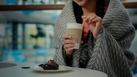 Photo for Unknown visitor woman client shopper girl rest at cafe restaurant cafeteria after shopping day wears blanket drinking aroma hot coffee tea from cup ordering chocolate cake enjoy delicious sweet desert - Royalty Free Image