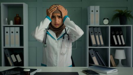 Téléchargez les photos : Malade arabique musulmane femme surchargée travailleur médical fatigué médecin médecin souffrent de maux de tête toucher la tête frotter tempes se sentir mal douleur migraine chronique maladie santé maladie due surmenage à l'hôpital - en image libre de droit