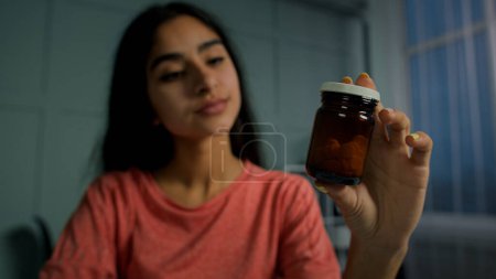 Foto de Joven árabe mujer española sostiene botella con pastillas medicación leer prescripción médica. Paciente enferma mujer tomar medicamentos prepararse para beber pastillas analgésicos medicamentos para el aborto o la salud inmunidad - Imagen libre de derechos