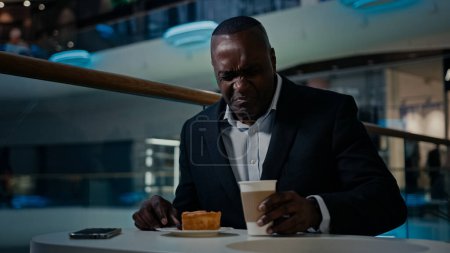 Téléchargez les photos : Afro-américain homme d'affaires d'âge moyen entrepreneur café visiteur homme assis manger à la cafétéria insatisfait de mauvais gâteau dégoût tarte dessert trouble boisson méchant thé insipide café désagréable - en image libre de droit