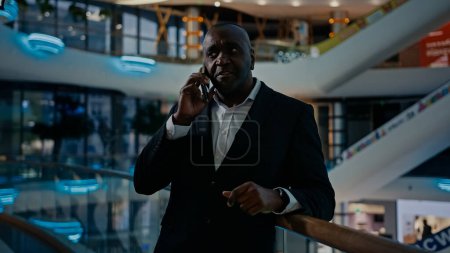 Photo for 50s advisor man phone call colleagues business partner talking with smartphone indoors in office company pointing direction explaining. African entrepreneur businessman calling answer talk cellphone - Royalty Free Image