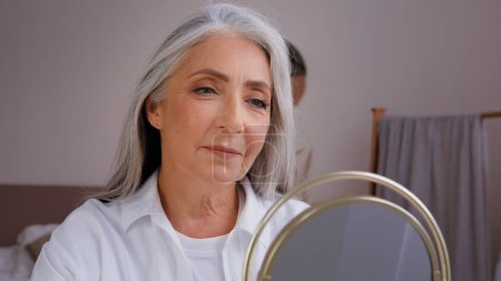 Close up old senior mature lady granny model enjoy shampoo recovery result 60s years aged Caucasian woman recovery long hair touching healthy gray silver hairdo haircare procedure looking at mirror