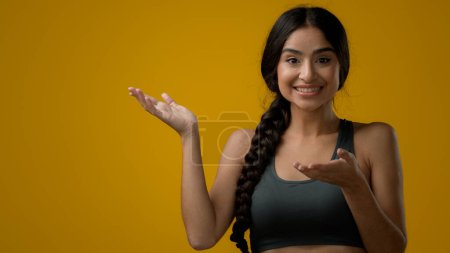 Téléchargez les photos : Satisfait femme indienne fille femelle regardant la caméra en studio fond jaune pointant vers côté vide espace de copie publicité étonnement étonnant regardant de côté étonnement incrédulité choc excité - en image libre de droit