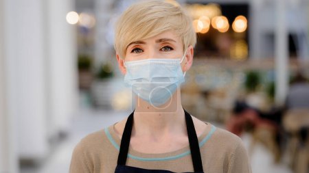 Photo for Portrait middle-aged woman adult lady cafe worker 40s female coffee shop owner waitress in protective medical face mask posing indoors looking at camera small business at epidemic coronavirus pandemic - Royalty Free Image