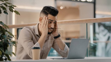 Photo for Sad shocked stressed ethnic CEO Indian man worker manager freelancer entrepreneur manager in cafe has problem with laptop app reading bad news worried with email shock stress business failure lost job - Royalty Free Image