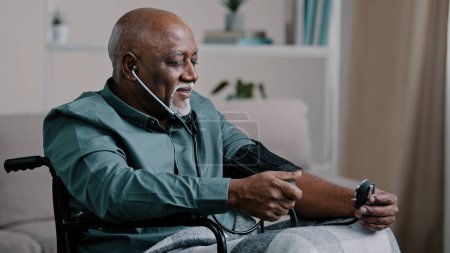 Foto de African old man elderly grandfather sitting in wheelchair measuring high low blood pressure mature male patient at home examining hypertension sufferer using medical tonometer cardiology healthcare - Imagen libre de derechos