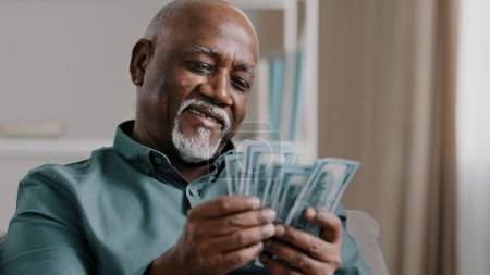 Téléchargez les photos : Happy african american satisfied winning bet elderly retired man counting savings mature male with pile dollars counting banknotes successful business investment profit in currency comfortable old age - en image libre de droit