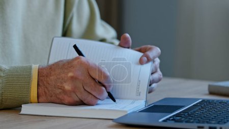 Photo for Unrecognizable mature man sit at workplace professor preparing lecture for students remote presentation author create handwritten text pensioner with wrinkles hands make notes writes memories in diary - Royalty Free Image