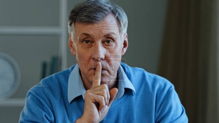 Photo for Closeup old caucasian 60s man holding index finger near mouth stop talking hush gesture silence sign elderly mature adult male telling secret looking at camera quietly showing forefinger send air kiss - Royalty Free Image