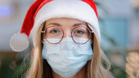 Photo for Close up female portrait Caucasian woman lady girl nurse doctor wearing red Santa Christmas hat cap and eyeglass and protective medical face mask New Year xmas pandemic coronavirus covid ill sick - Royalty Free Image