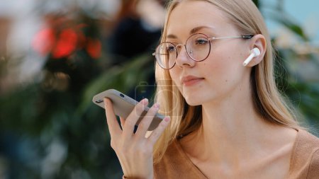 Foto de Close up emotional girl use virtual assistant speak in microphone of phone caucasian young lady with glasses talk on speakerphone record audio message using wireless headphones telephone communication - Imagen libre de derechos