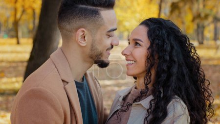 Photo for Multiracial ethnic Hispanic happy married couple in love standing outdoors man and woman boyfriend and girlfriend wife and husband looking at each other with tenderness affectionate in autumn park - Royalty Free Image