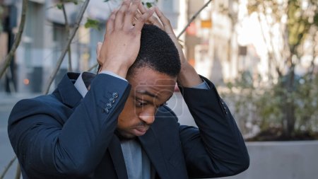 Photo for Stressed exhausted ethnic man male guy company employee having painful head pain headache stress with lost job fired unemployment in city. Tired African American man businessman overwhelmed outdoors - Royalty Free Image
