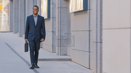 Foto de African American man ethnic smiling happy businessman employer entrepreneur boss leader worker investor lawyer male guy company CEO manager in business suit with suitcase walking in city walk outdoors - Imagen libre de derechos