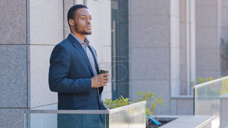 Téléchargez les photos : African American businessman pensive relaxed thoughtful entrepreneur office worker manager man guy male employer standing on balcony pondering business strategy think with tea coffee thinking relaxing - en image libre de droit