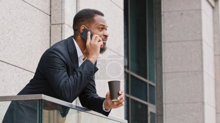 Photo for Serious bearded African American millennial businessman entrepreneur man ethnic manager talking mobile phone standing on office balcony male executive speak by cellphone business call negotiation - Royalty Free Image