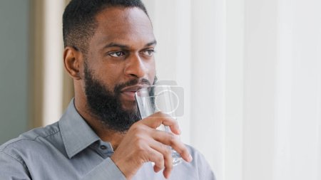 Téléchargez les photos : Adult beaded African American guy company CEO boss leader employee entrepreneur man ethnic businessman with glass drink cold water. Healthy worker hydrating thirst drinking at workplace aqua balance - en image libre de droit