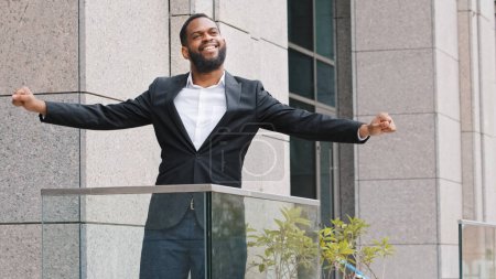 Photo for Overjoyed happy funny cheerful African ethnic American male employee entrepreneur businessman worker man standing on office balcony dancing relaxing celebrate business success reward corporate success - Royalty Free Image