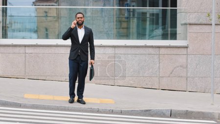 Foto de African American man ethnic businessman talking phone answer call talk with smartphone conversation with business partner client discussing offer speak with telephone cellphone phone in city outdoors - Imagen libre de derechos