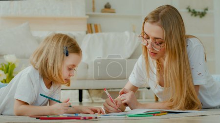 Petite enfant adopté petite fille profiter dessin d'art avec mère caucasienne dans des lunettes couchées à la maison plancher ensemble. Fille bébé enfant avec maman maman baby-sitter professeur dessin image avec crayons parler