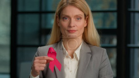 Foto de Headshot portrait Caucasian middle-aged woman hold red ribbon in office businesswoman with HIV AIDS awareness disease prevention protection sign volunteering activity charity. World breast cancer day - Imagen libre de derechos