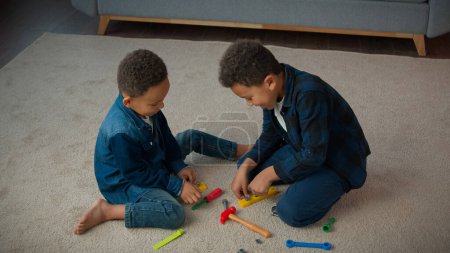 Téléchargez les photos : Ethnic African American multiracial multiethnic boys kids schoolboys pupils sons indoors at home children brothers cousins friends on floor carpet play with toys tools playing repair game together - en image libre de droit
