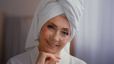 Photo for Headshot female portrait happy 50s middle-aged lady 60s mature woman touching facial skin looking at camera with smile touch face pampering wears towel on head enjoy cosmetics and plastic surgery - Royalty Free Image