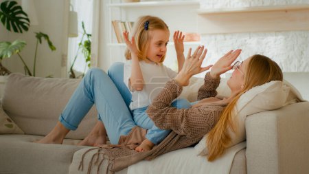 Photo for Happy parent Caucasian mom mother with cute kid daughter child girl baby playing patty cake game at home clapping hands lying on sofa couch at home living room carefree family having fun play together - Royalty Free Image