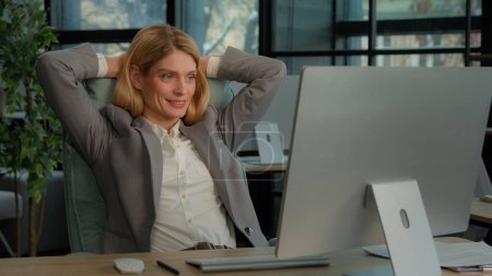 Photo for Middle-aged adult Caucasian woman 40s satisfied businesswoman finished computer work stretching sitting at workplace. Relaxed office worker female relax rest after job well done with hands behind head - Royalty Free Image