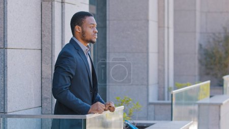 Téléchargez les photos : African American man pensive serious dreaming relaxed thoughtful employee taking break from work in office standing on balcony ethnic businessman male thinking contemplate looking away at cityscape - en image libre de droit
