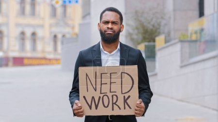 Photo for Sad frustrated hopless fired African American man ethnic upset guy worker in city holding poster need work help searching job offer jobless crisis unemployment business lost bankrupt loosing career - Royalty Free Image