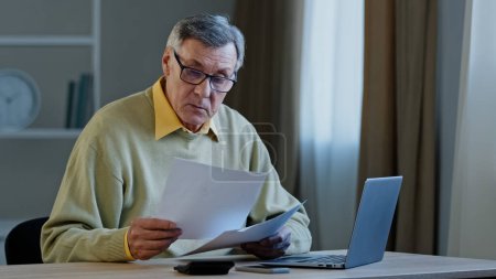 Photo for Worried puzzled old caucasian grey-haired businessman 70s male sad man sitting at table with paperwork problems with documents mistake finance budget checks data has conference video call. High - Royalty Free Image