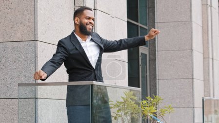 Téléchargez les photos : Happy funny cheerful African ethnic entrepreneur executive celebrate good news winning victory with funny dance. American employee man entrepreneur businessman on office balcony dancing in morning - en image libre de droit