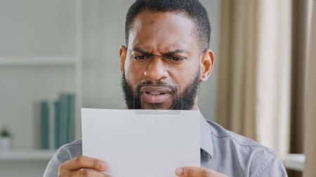 Foto de Unhappy African American bearded guy man received bad news reading letter with bank refuse feeling stressed about dismissal notice. Angry sad ethnic businessman read credit loan refusal notification - Imagen libre de derechos