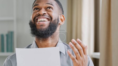Foto de Bearded African American adult male worker manager entrepreneur employer receive letter mail paper notice of bank loan approval salary offer. Ethnic guy man reading good news celebrate victory achieve - Imagen libre de derechos