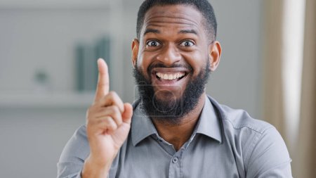 Photo for Happy exited bearded African American ethnic man entrepreneur businessman worker manager in office looking at camera rise forefinger index finger come up with good idea find answer perfect solution - Royalty Free Image