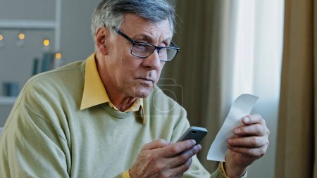 Téléchargez les photos : Caucasian old 60s man senior mature grandfather holding smart phone using mobile e-bank application. calculating accounting bills budget with paper financial check using calculator app in telephone - en image libre de droit