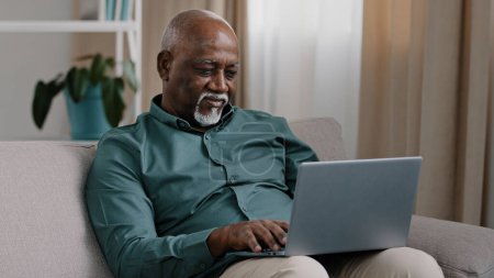 Téléchargez les photos : Older bald African American man 60s senior mature businessman use easy wireless technology for comfort work online shopping ecommerce at home couch typing massage chatting banking in computer app - en image libre de droit