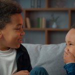 Two little boys friendly talking laughing at home. Ethnic African American multiracial multiethnic male kids schoolboys pupils sons indoors talk laugh together. Children brothers friends conversation
