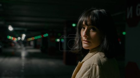 Téléchargez les photos : View from behind close up headshot portrait Caucasian woman female lady girl standing at dark empty dangerous parking lot turning back looking at camera with calm face scare afraid in underground - en image libre de droit