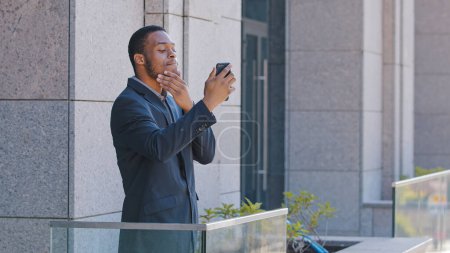 Téléchargez les photos : African American office worker man standing on balcony take picture shooting video blog make selfie photo for vlog blogger guy speaking with followers with smartphone video chat app with mobile phone - en image libre de droit