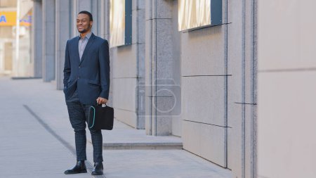 Photo for African American man ethnic businessman employer entrepreneur employee boss leader manager investor company CEO male guy in business suit with suitcase in city outdoors on street standing waiting taxi - Royalty Free Image