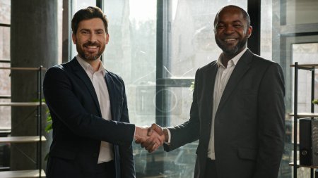 Photo for Two happy smiling diverse multiracial businessmen multiethnic partners men Caucasian and African American business people in office shaking hands smiling handshake agreement handshaking partnership - Royalty Free Image