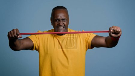 Photo for Mature athletic man stand in gray background studio strong athlete sportsman with tense expression stretches elastic band using sports equipment demonstrates power muscles bicep workout sport concept - Royalty Free Image