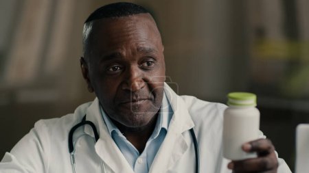 Téléchargez les photos : Homme médecin homme mûr afro-américain soignant médecin infirmier tenir bouteille avec des comprimés médicaments analgésiques pilules antibiotique supplément pharmaceutique pour l'immunité donner un traitement médicamenteux de santé - en image libre de droit