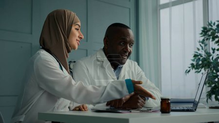 Photo for Medical people two professional doctors colleagues arabian young woman therapist discuss electronic health test results with african senior man use computer application doing online digital diagnostic - Royalty Free Image