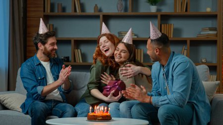 Photo for Excited woman receive gift present from friends diverse multiracial colleagues congratulate wish happy birthday presenting surprise box. Ethnic women men in party caps have fun celebrate event at home - Royalty Free Image