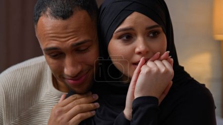 Foto de African american man care about sad offended crying arabian muslim woman diverse multiracial couple sit indoors loving husband calming wife cuddling apologize support empathy family relation problem - Imagen libre de derechos