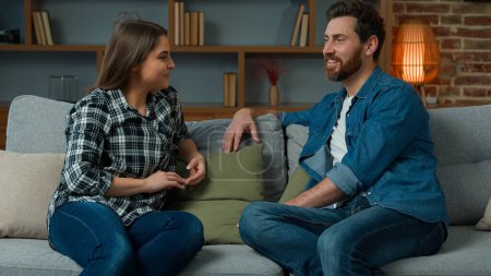 Téléchargez les photos : Young couple caucasian hispanic partners husband and wife sit on sofa female woman talk with male friend bearded man talking indoors gossiping friendly dialogue discussing future plans together family - en image libre de droit