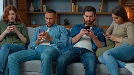 Photo for Focused four diverse african american caucasian hispanic friends sit on sofa in living room look at mobile screen together phone gadget internet addicted men women ignoring each other boring meeting - Royalty Free Image
